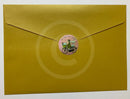 A square gold envelope with a pointed flap, sealed with a round pink sticker featuring a bicycle illustration and the text 'Go Your Own Way'.