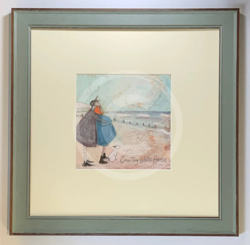 Meet the Mustards: Counting White Horses by Sam Toft, mounted miniature print. A couple on a beach with a black and white dog embracing, and looking up a the clouds.  Framed in Nordic Blue.