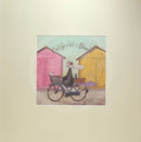 Meet the Mustards: Out For a Bit of Brunch by Sam Toft, mounted miniature print. A man rides on a bicycle with his dog sat in the front basket, they have a picnic basket on the back. They are riding past two pink and yellow beach huts. 