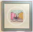 Meet the Mustards: Out For a Bit of Brunch by Sam Toft, mounted miniature print. A man rides on a bicycle with his dog sat in the front basket, they have a picnic basket on the back. They are riding past two pink and yellow beach huts. Framed in Nordic Blue. 