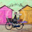 Meet the Mustards: Out For a Bit of Brunch by Sam Toft, mounted miniature print. A man rides on a bicycle with his dog sat in the front basket, they have a picnic basket on the back. They are riding past two pink and yellow beach huts. 