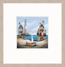 The Blue Lagoon by Gary Walton — two clusters of wonky coastal cottages with teal window frames either side of a sheltered lagoon, red and white lighthouse on the headland, sailboat on the vivid blue water and wooden rowing boat beached in the sandy foreground - oak effect frame option