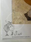 A close-up of a printed artwork or book/poster page showing a black sketch of two figures and a small dog on a white page, alongside a textured tan painted section. Visible text reads 'The Unexpected Smackero!' by Sam Toft.