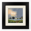 Towards the Evening Light by Allan Morgan — a narrow path through a meadow of blue flowers towards distant trees beneath a blue-grey sky glowing with soft peach-gold light, presented in a broad matt black frame with an off-white inner slip frame